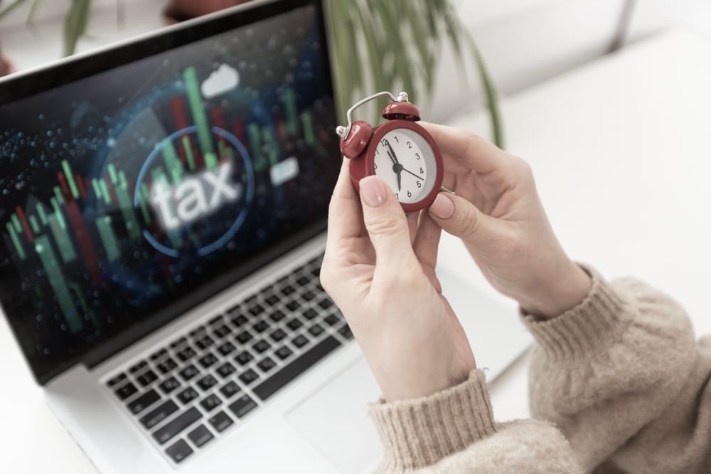 Woman holding a tiny clock while her laptop screen displays the word tax
