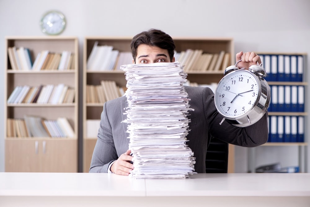 Office worker holding a clock, covered by a tall stack of documents