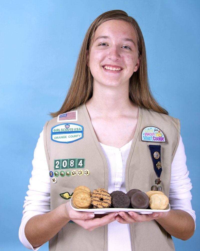 Girl Scout in uniform holding a tray of cookies