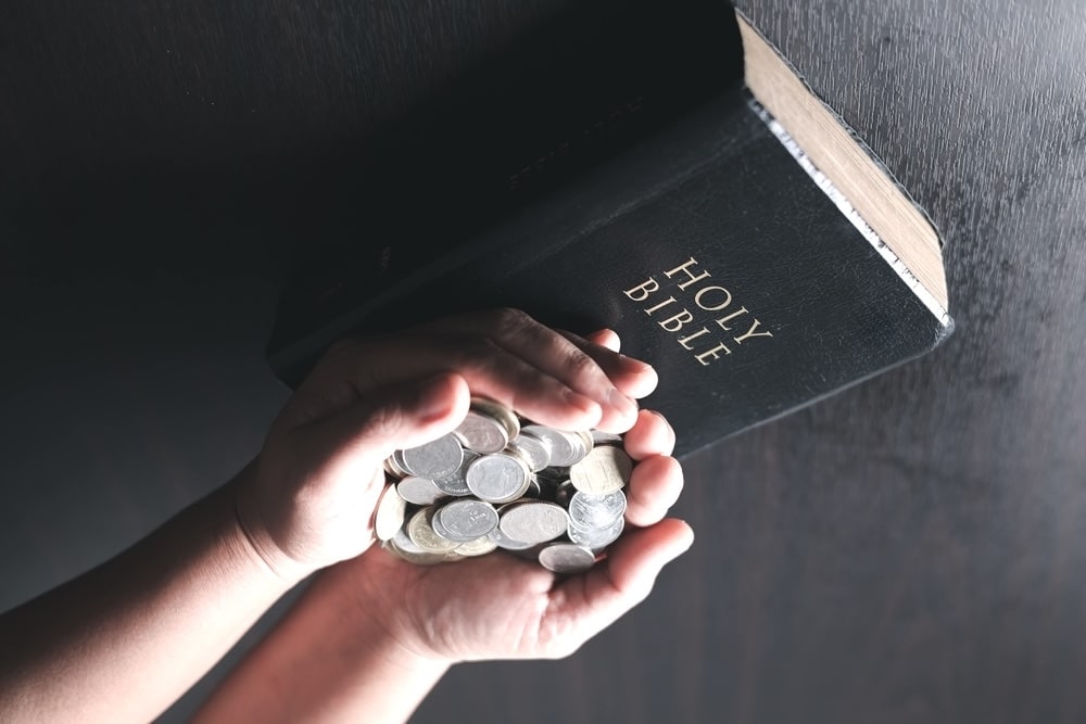 Hands filled with coins on top of a black Holy Bible