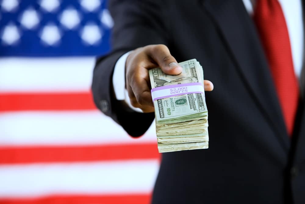 Hand holding a pile of cash for a political donation with American flag behind him